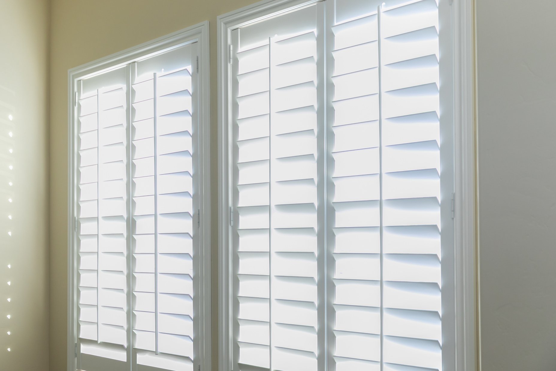 A set of open white plantation shutters in a light butter yelllow room